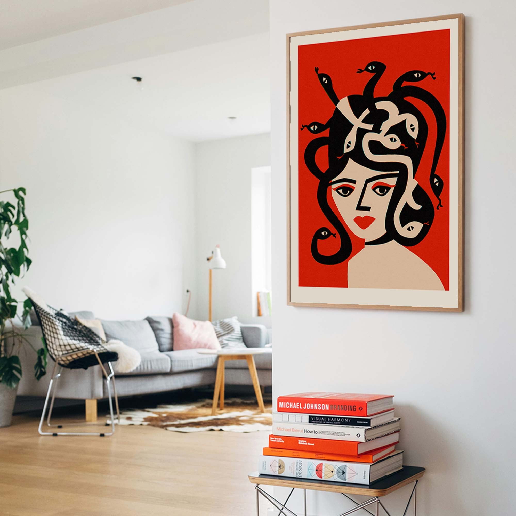 A framed art print featuring a stylized illustration of Medusa with black snakes in her hair, hanging on a white wall in a modern living room setting.