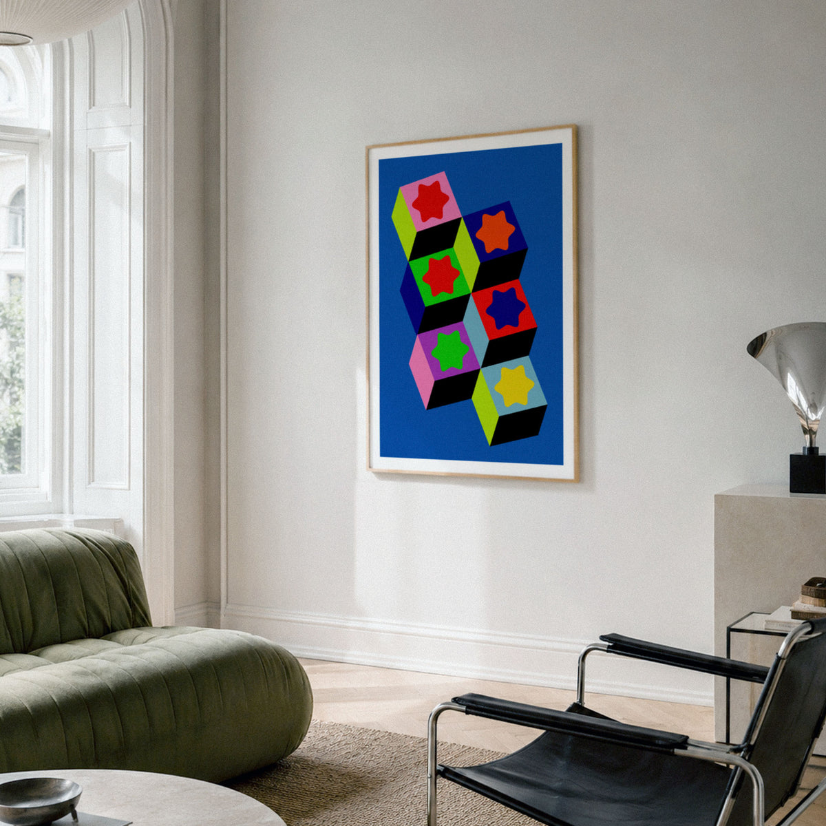 A framed pop art print featuring colorful geometric 3D cubes on a blue background, displayed on a light gray wall in a modern living room setting.