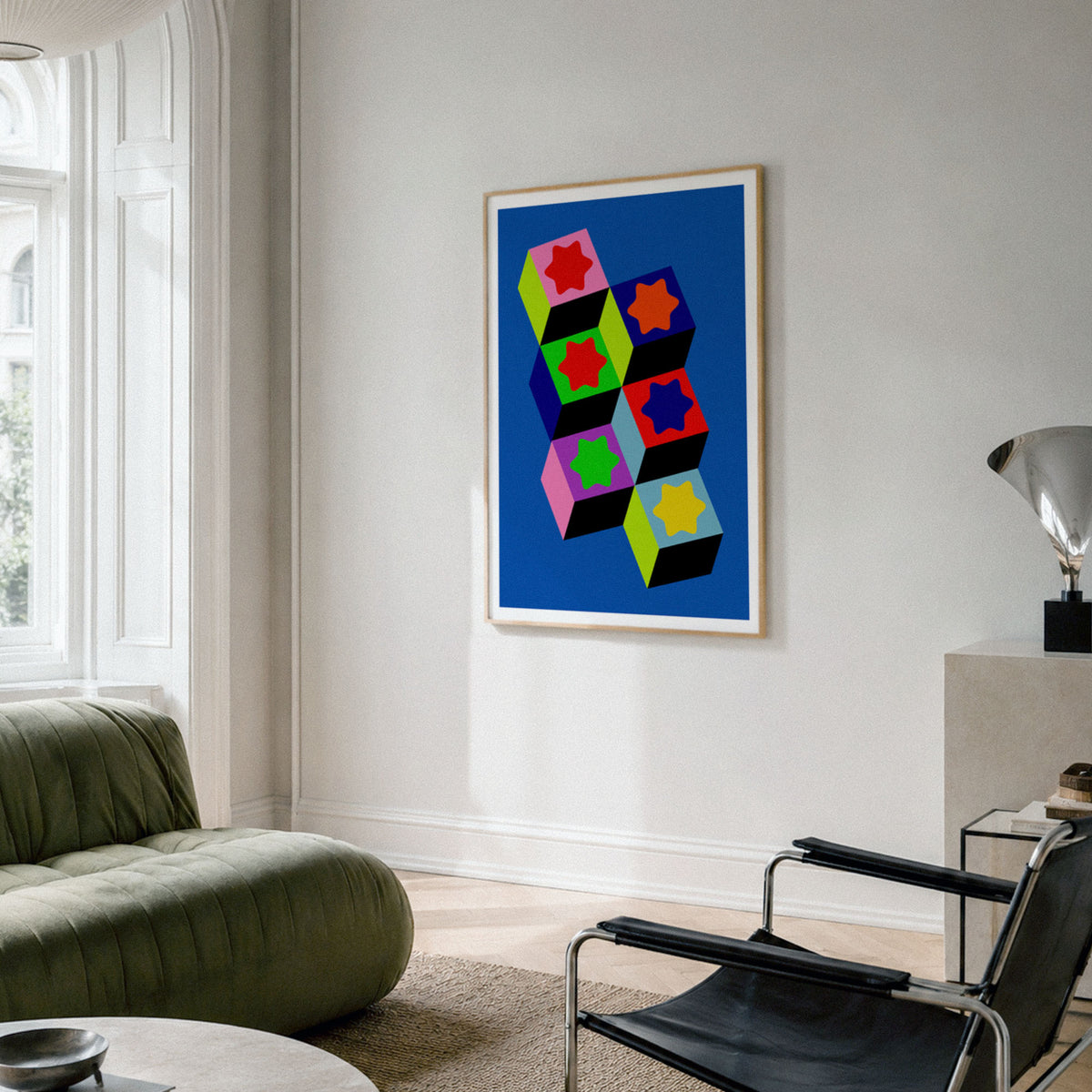 A framed pop art print featuring colorful geometric 3D cubes on a blue background, displayed on a light gray wall in a modern living room setting.