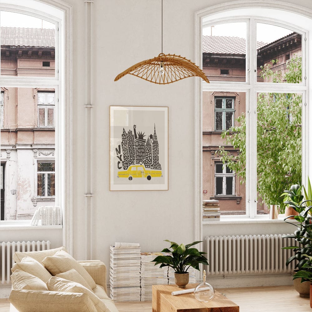 Framed NYC print featuring towering black buildings and a yellow cab, shown hanging in a bright, modern room with wood accents and leafy plants.