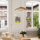 Framed NYC print featuring towering black buildings and a yellow cab, shown hanging in a bright, modern room with wood accents and leafy plants.