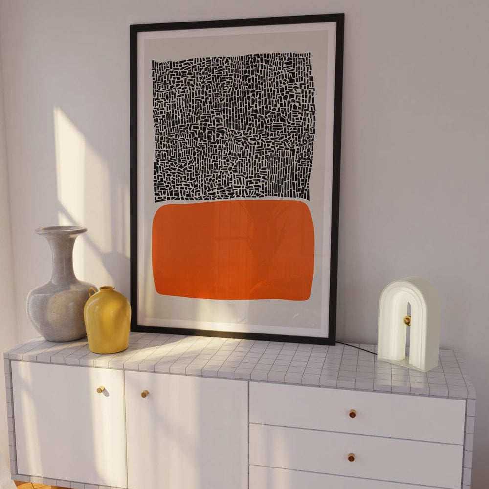 Framed abstract orange block print displayed in a stylish room with minimalist white furniture, warm lighting, and subtle sculptural decor.