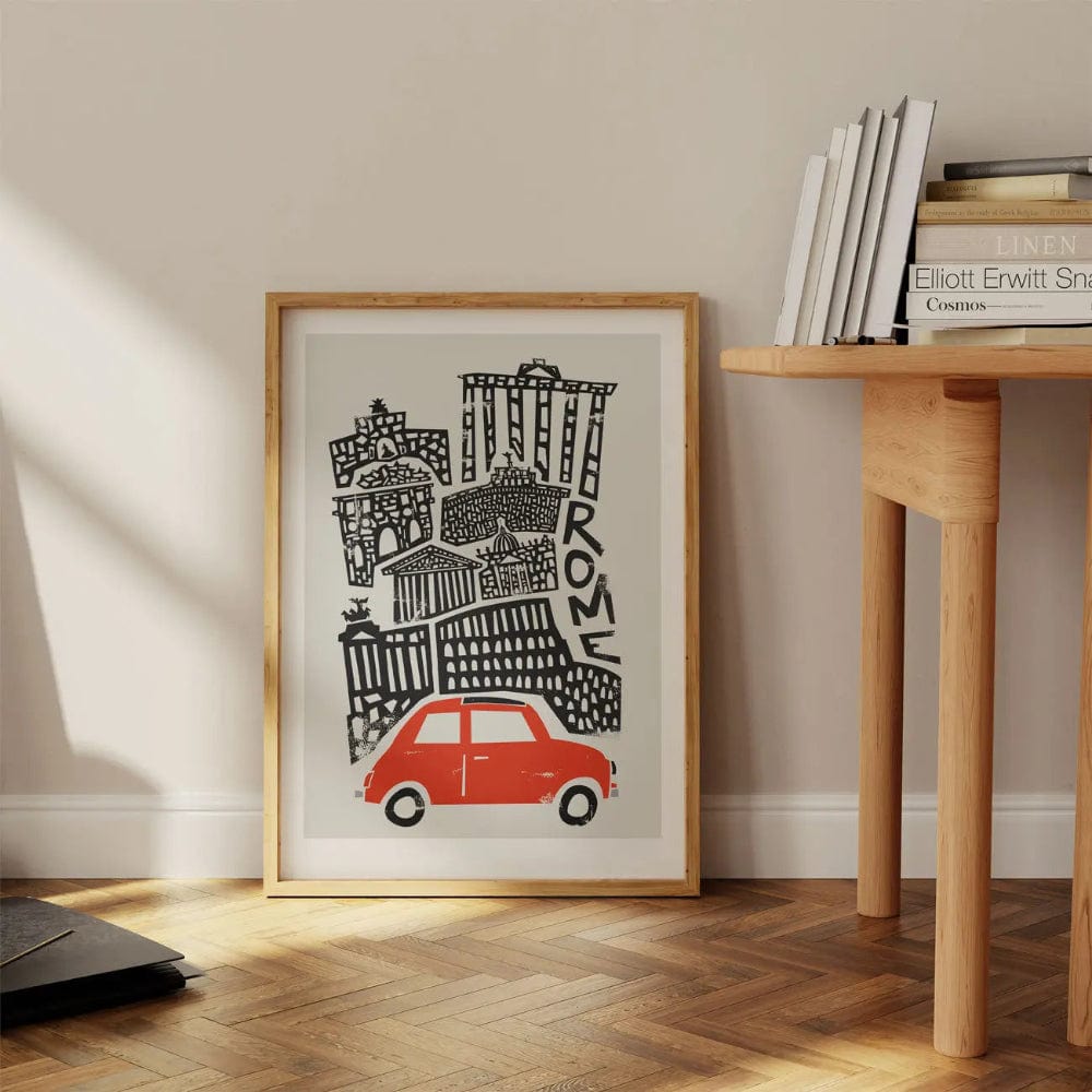 Framed Rome city print with red Fiat resting on the floor near a wooden desk—mid-century line work meets warm nostalgic charm in a modern space.