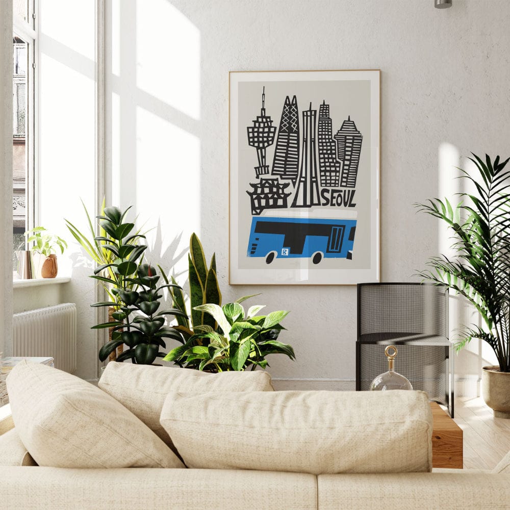 Seoul city print framed above a cream sofa surrounded by indoor greenery in a bright, modern space.