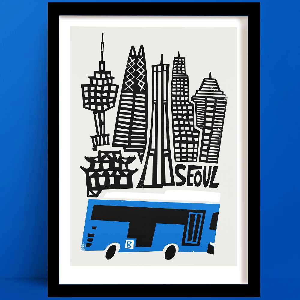 A Seoul print featuring bold black-and-white architectural silhouettes above a stylised blue city bus, framed on cobalt wall.