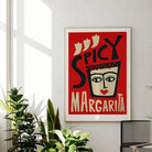 The Spicy Margarita print brings fire and flair to a minimalist room, framed in black and glowing in natural sunlight against a clean white wall.