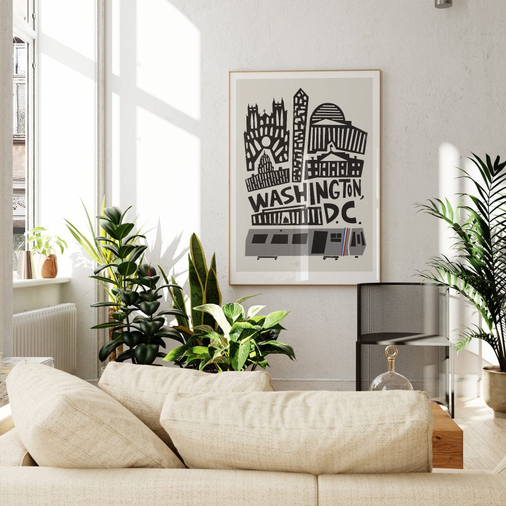 Framed D.C. city artwork above a neutral-toned sofa, styled with leafy green plants in a light-filled, modern interior.
