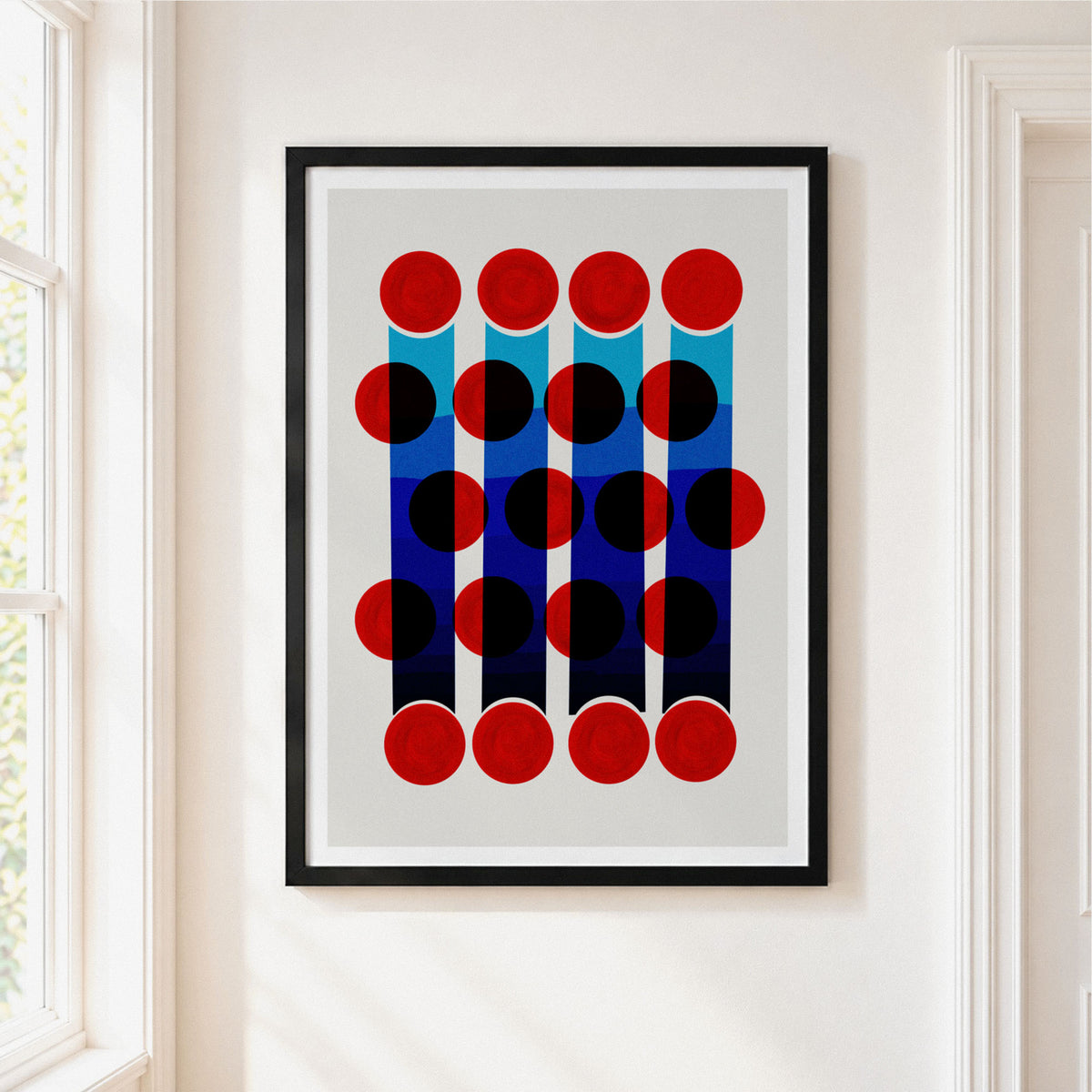 Framed abstract geometric wall art hanging on a white wall, featuring red and black circles over vertical blue and navy bars on a light gray field, with a black frame visible.