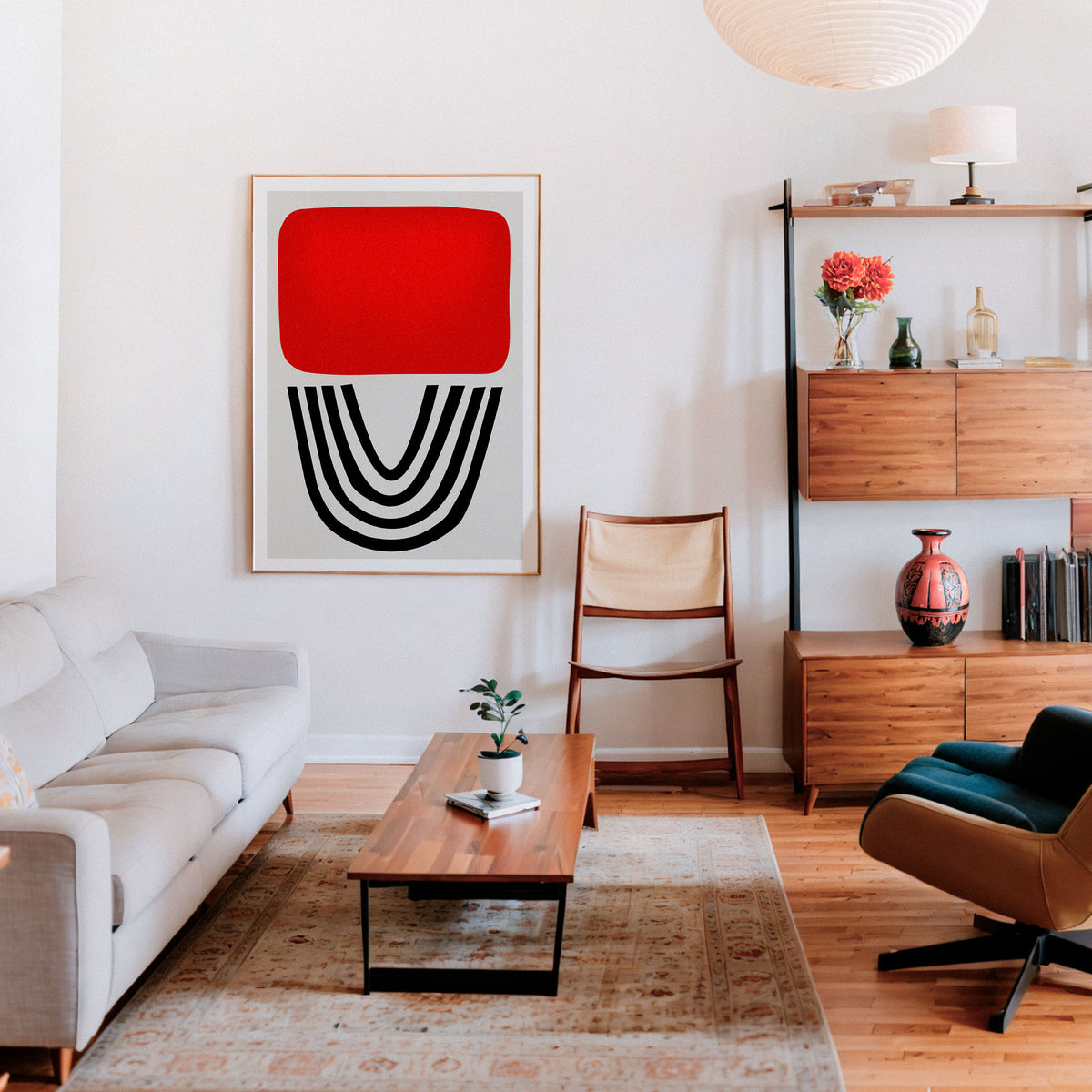 A modern living room featuring a large framed abstract art print on the wall. The print has a bold red rectangle at the top and black curved lines below, set in a light wood frame.