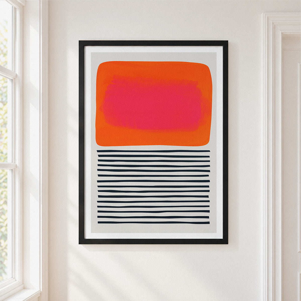 A framed abstract art print 'Sunset Ripples' hanging on a white wall in a bright room. The print features a large orange and pink rounded rectangle on the upper half and horizontal black stripes on the lower half, enclosed in a thin black frame.