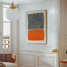 A framed abstract art print 'City Sunset' featuring a black and white patterned top half and a solid orange bottom half, hanging on a white paneled wall in a bright, modern room.