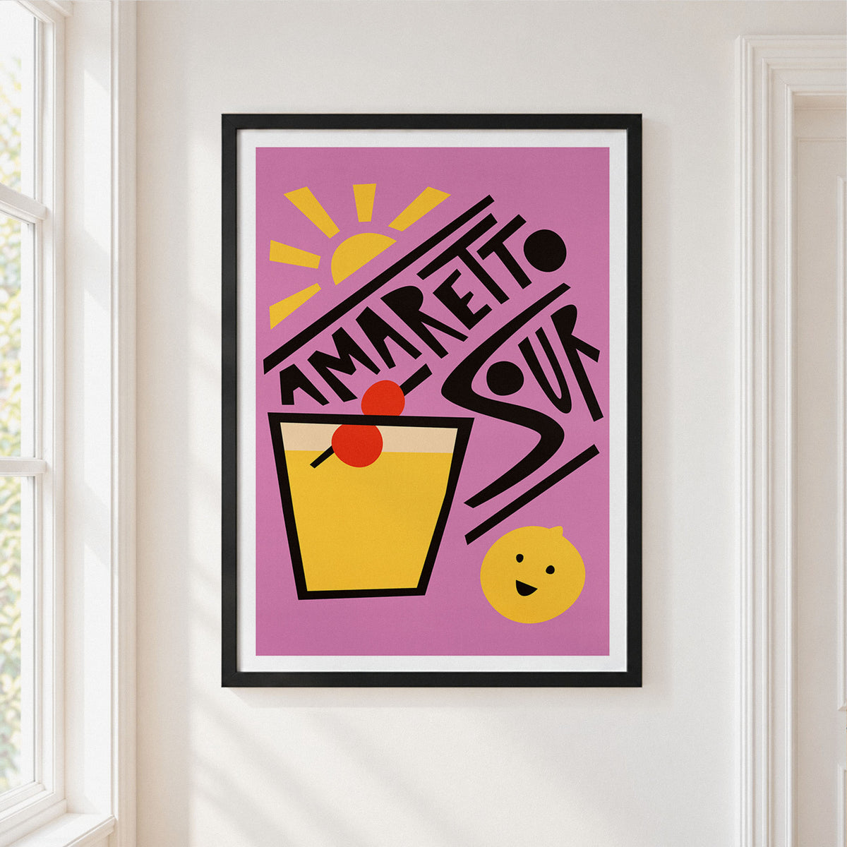 A framed art print featuring a retro-style illustration of an Amaretto Sour cocktail on a pink background, hung on a white wall next to a window.