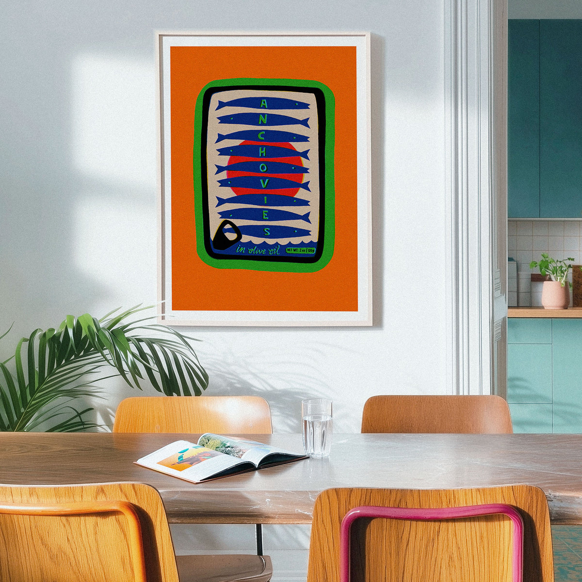 A framed art print featuring a retro fish pattern in orange, blue, red, green, and cream, hanging on a light gray wall above a wooden dining table with chairs in a modern kitchen setting.