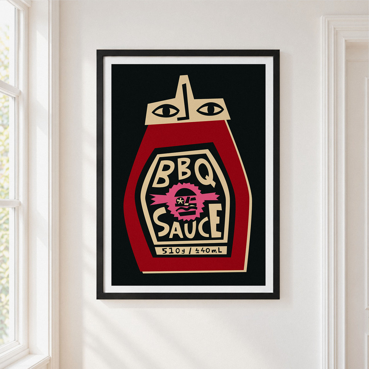 A framed art print of a stylized ketchup bottle labeled 'BBQ SAUCE' hanging on a white wall next to a window.