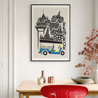 A framed travel poster of Bangkok hanging on a light gray wall above a wooden table with decorative vases, a bowl, and a red chair. The poster features a black and white illustration of Bangkok landmarks and a blue-and-yellow tuk-tuk, with the word 'BANGKOK' written vertically.