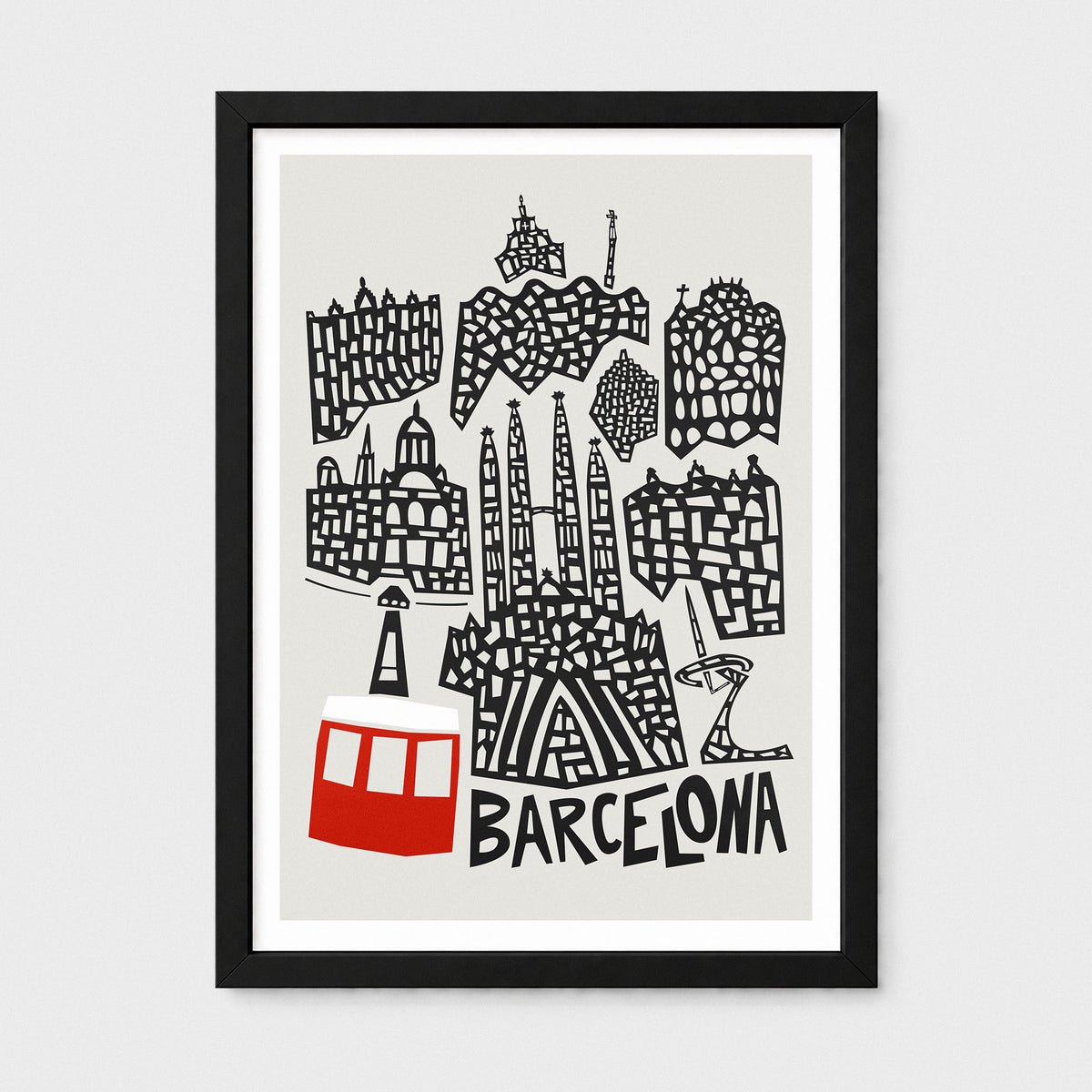 A framed art print featuring a black and white hand-drawn illustration of Barcelona landmarks, including Sagrada Familia and the Park Güell cable car, on a light gray background with the word 'BARCELONA' at the bottom. The print is framed in black with a white mat, set against a light gray wall.
