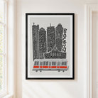 A framed art print featuring a stylized black and white Boston skyline with a red and gray cable car, hanging on a white wall next to a window.