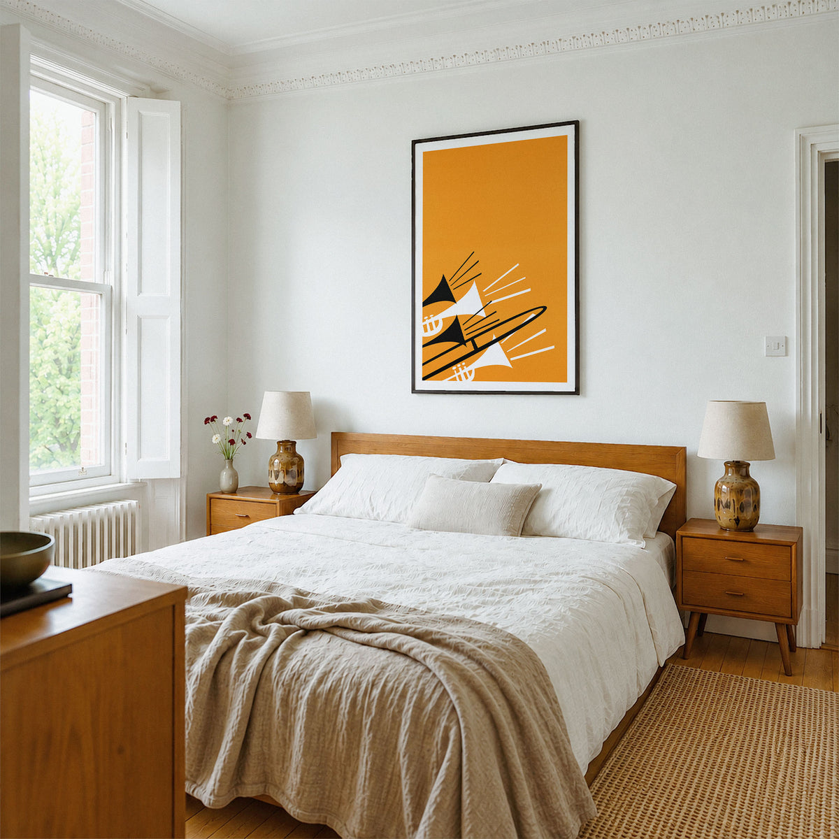 A modern bedroom featuring a prominent vertical framed art print with an orange, black, and white geometric design above a wooden bed. The room has white walls, a wooden headboard and nightstands, white lamps, and a beige textured throw blanket.