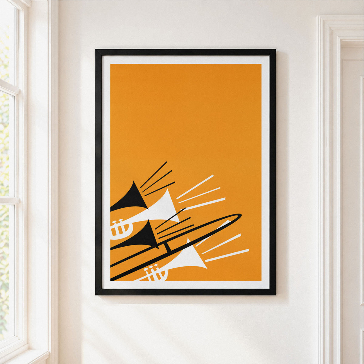A framed abstract art print featuring stylized jazz instruments in black, white, and orange, hung on a white wall next to a window.
