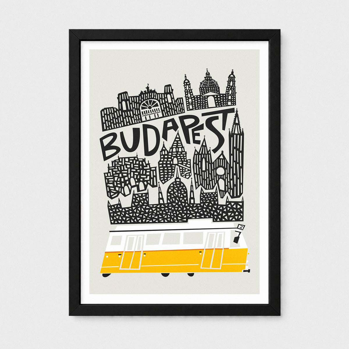 A framed Budapest travel art print featuring a black and white skyline illustration with the word 'BUDAPEST' and a yellow bus at the bottom, shown against a light gray background.