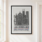 Framed Chicago cityscape wall art hanging on a cream wall beside a window. The print shows black-and-gray skyscrapers with the word CHICAGO and a gray, white, and blue train at the bottom, enclosed in a black frame.