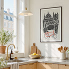 A framed art print featuring a black and white illustration of Copenhagen landmarks and a red bicycle, hanging on a light wall in a bright, modern kitchen.