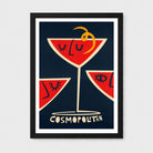 Framed art print featuring three red cocktail martini glasses with stylized faces and a yellow twist on a dark navy background, with the word 'COSMOPOLITAN' at the bottom. The print is framed in black with a white mat against a light gray wall.