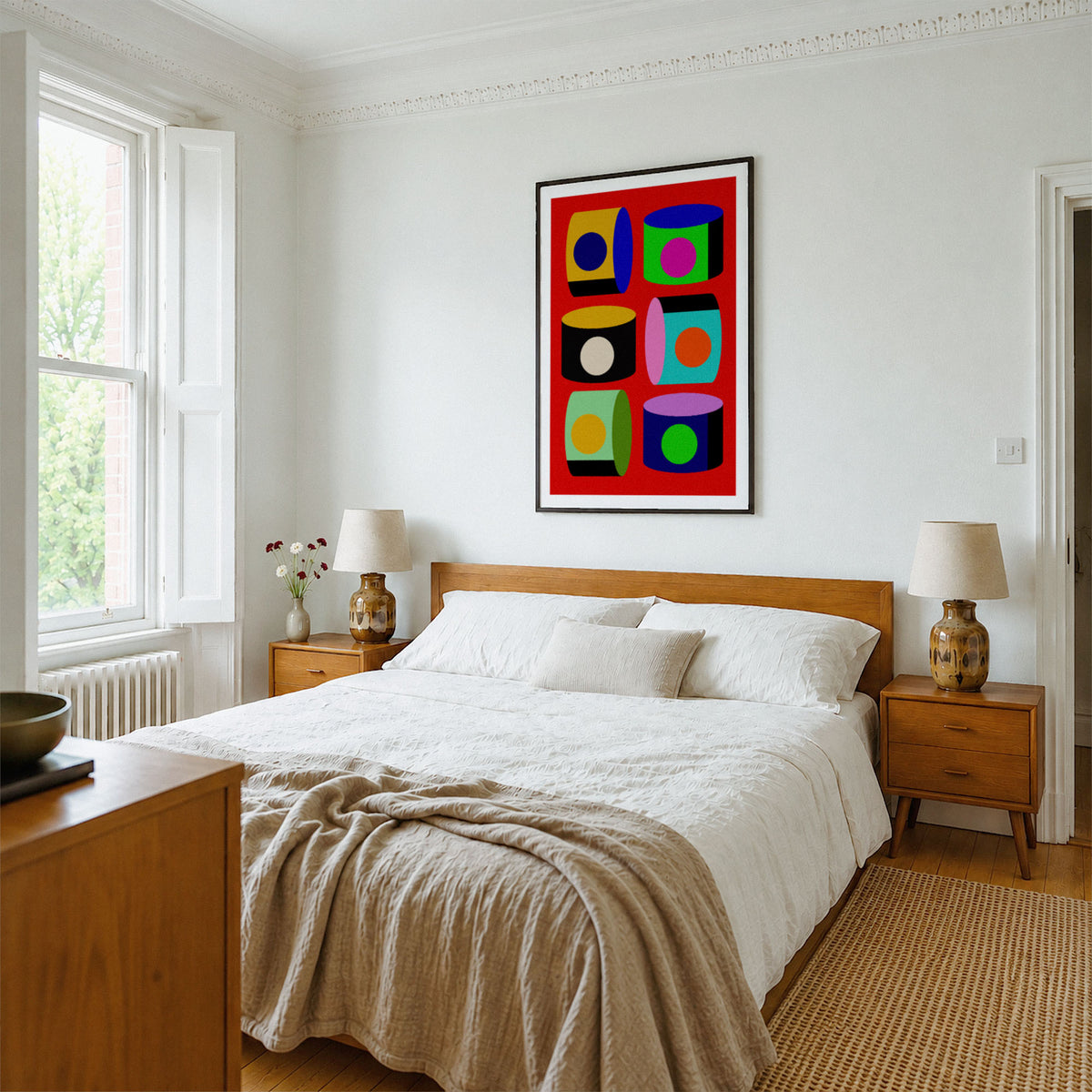 A colorful abstract wall art print with bold geometric shapes in red, green, yellow, blue, and black, displayed above a wooden bed in a bright, modern bedroom.
