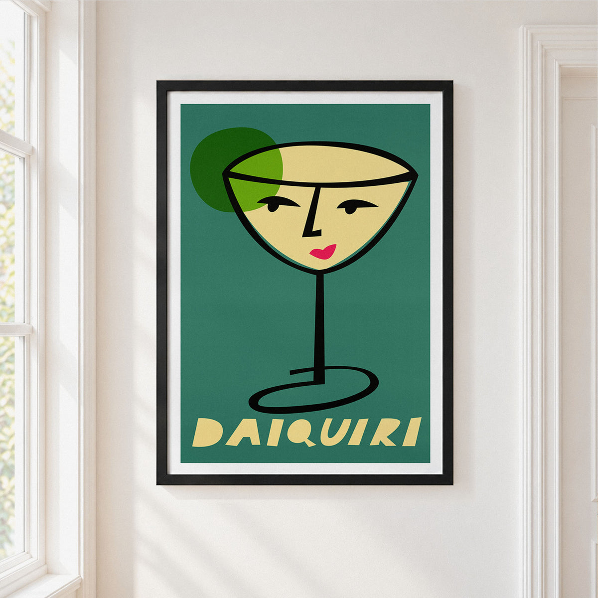 A framed art print featuring a stylized cocktail glass with a face and the word 'DAIQUIRI' at the bottom, hanging on a white wall next to a window.