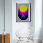 Framed abstract art piece on a wall above a white chair in a room.