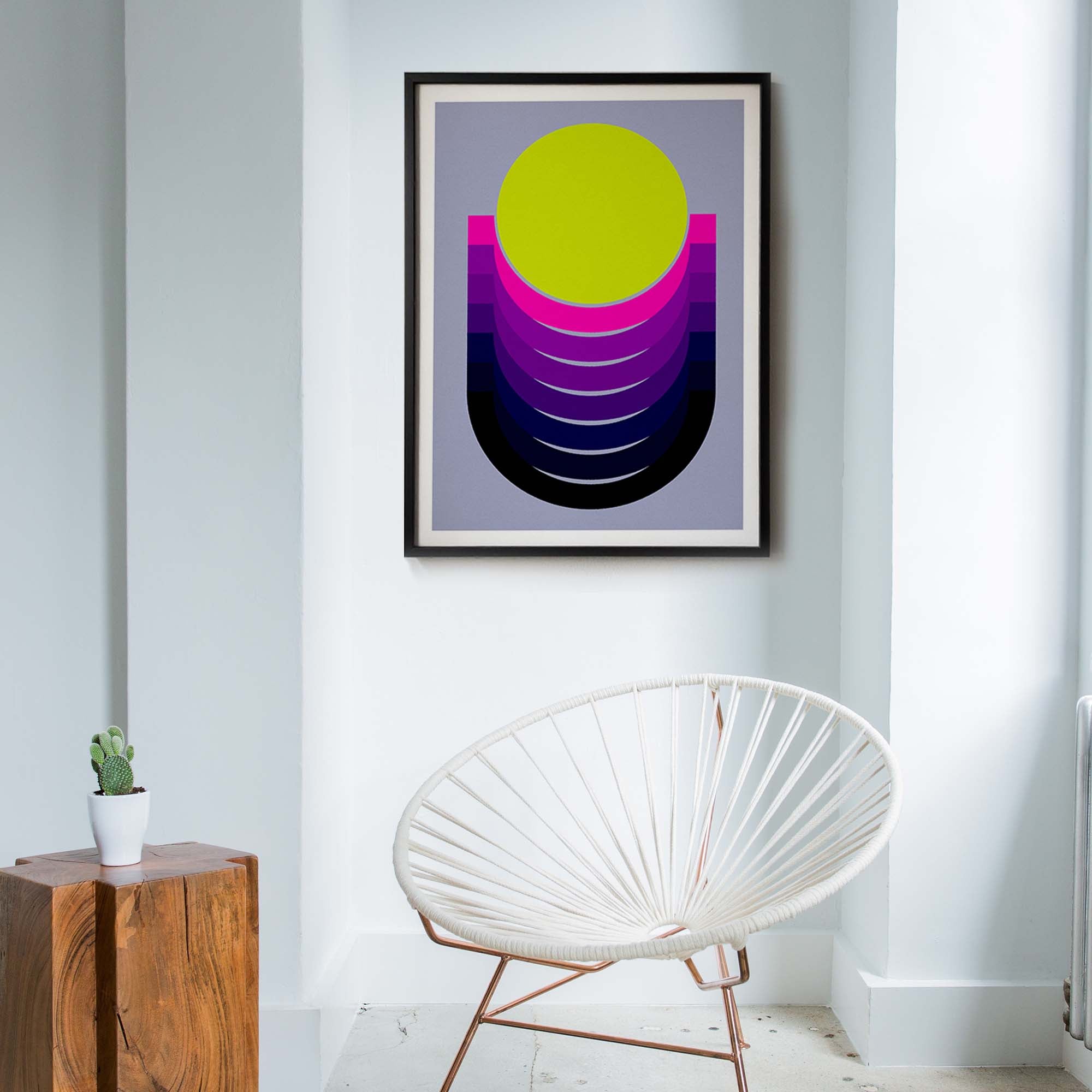 Framed abstract art piece on a wall above a white chair in a room.