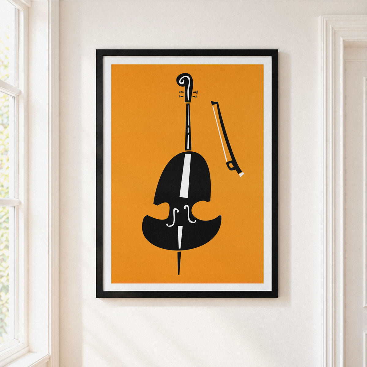Framed minimalist wall art featuring a black cello silhouette on a warm orange background, hung on a white wall beside a window.