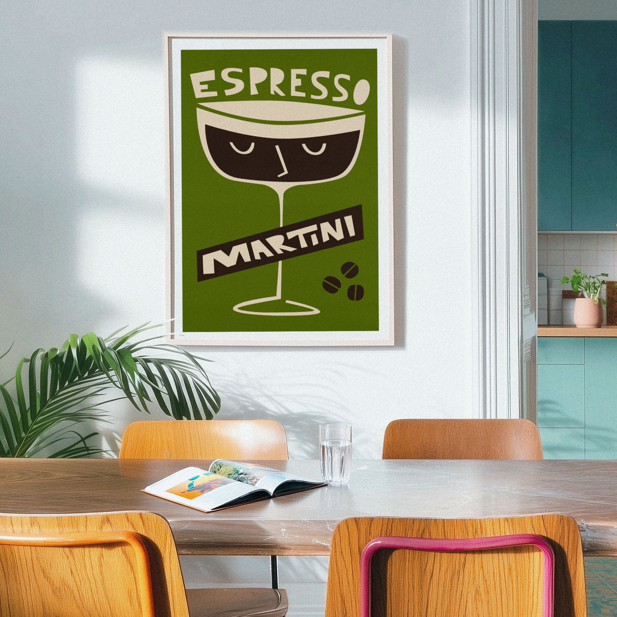 A framed vintage-style poster reading 'ESPRESSO MARTINI' hangs on a light wall above a wooden dining table with chairs in a real interior setting.