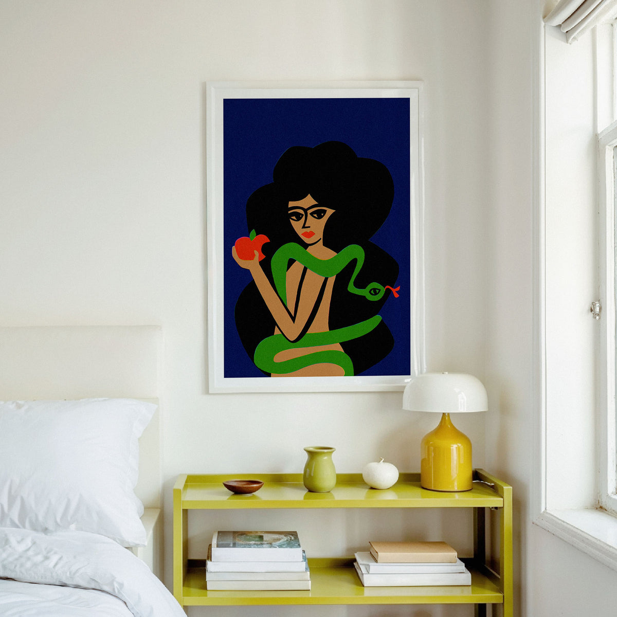 A framed art print featuring a stylized illustration of a woman with dark hair wrapped in a green snake and holding a red apple, displayed on a bedroom wall above a yellow bedside table.