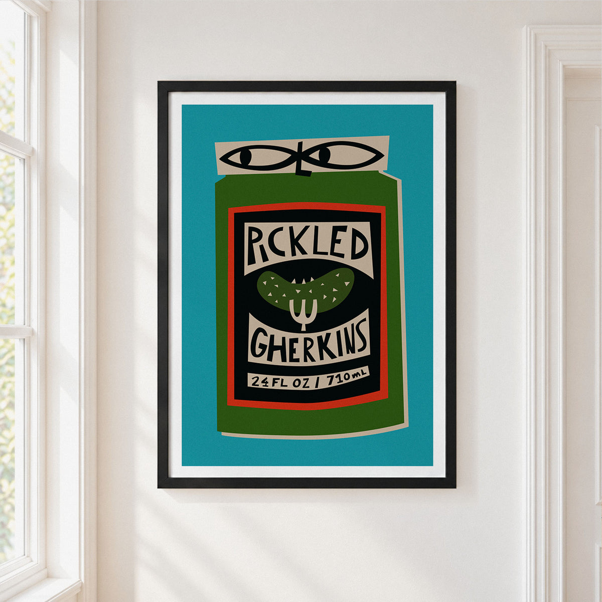 A framed art print featuring a stylized pickle jar labeled 'PICKLED GHERKINS' on a turquoise background, hung on a white wall next to a window.