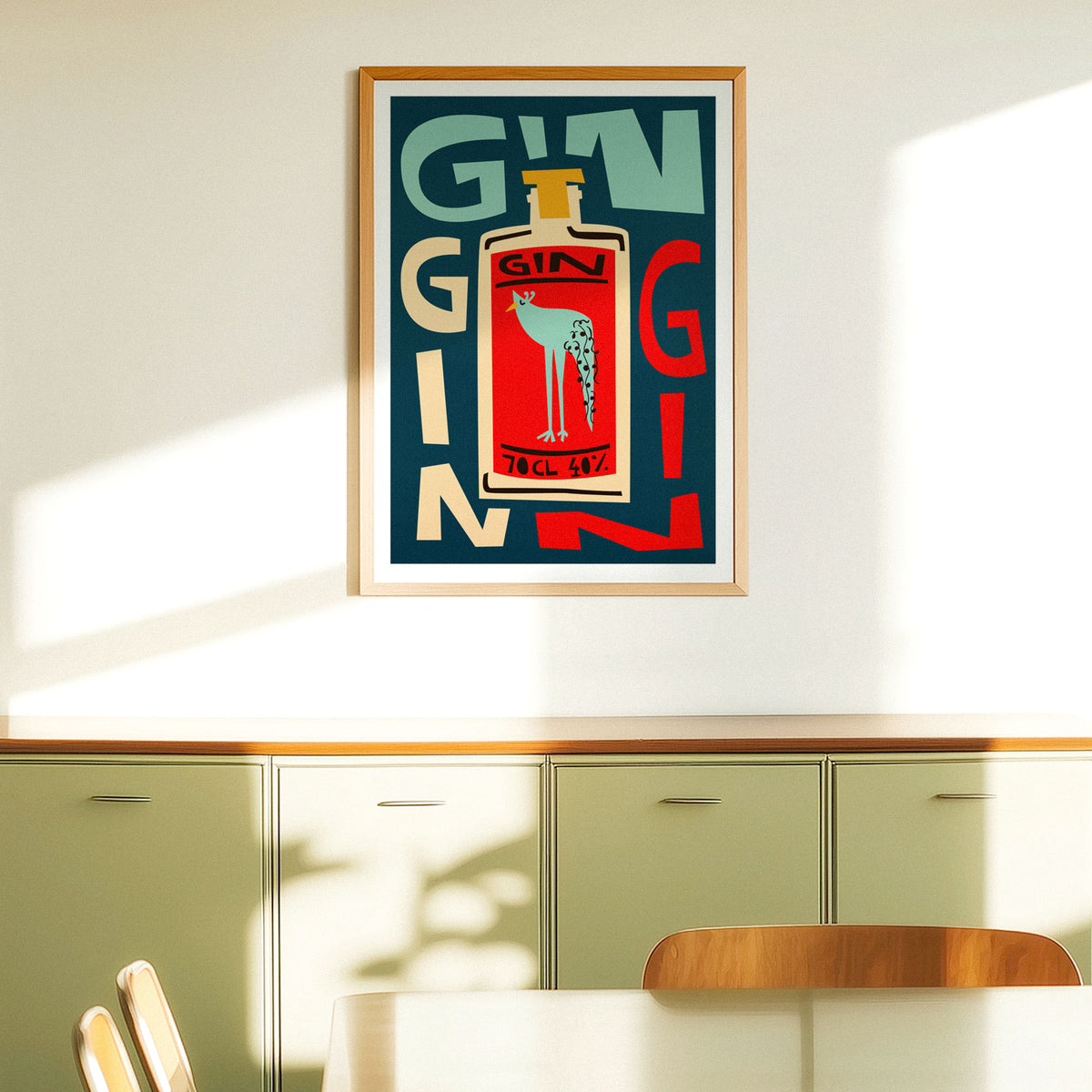 A framed vintage-style poster featuring a bold gin bottle illustration with the word 'GIN' in large letters, hanging on a light wall above green cabinets in a sunlit interior.