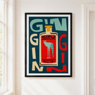 A framed art print featuring a retro-style illustration of a gin bottle with a bird on the label, mounted on a white wall next to a window.