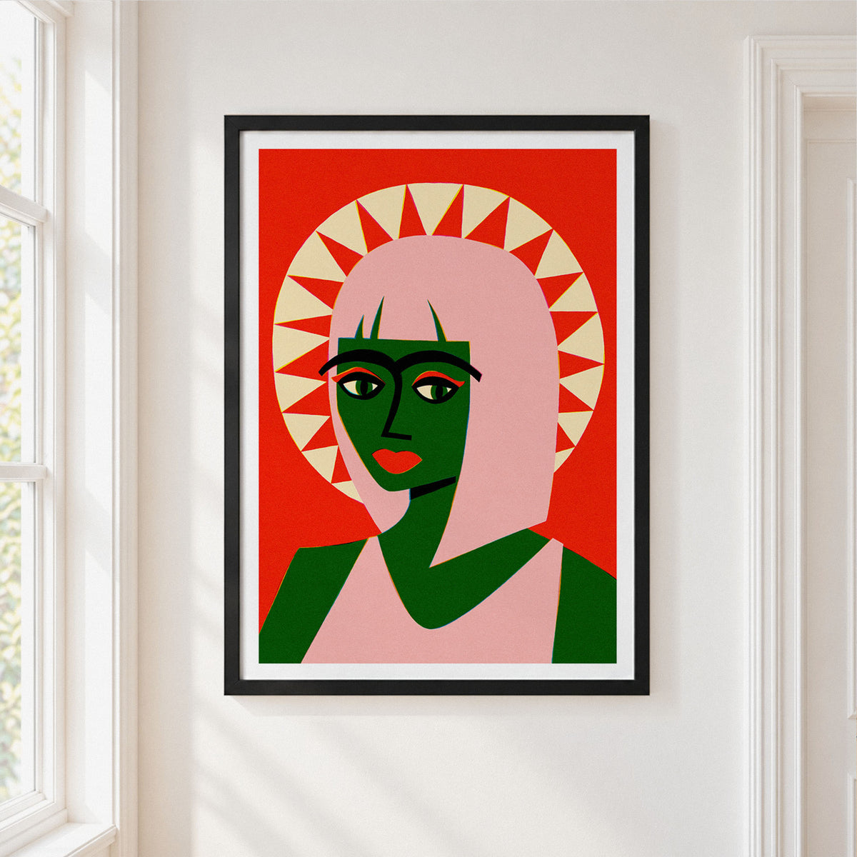 A framed art print featuring a stylized, mid-century modern portrait of a woman in green and pink against a red background, hanging on a white wall next to a window.