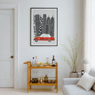 A framed art print featuring a black and white stylized cityscape of Hong Kong with a red car, displayed on a white wall in a modern living room setting above a wooden bar cart.