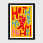 A framed art print featuring a bold retro illustration of some chilli's with the word 'HOT' repeated in red, pink, and blue on a bright yellow background, with a large red chili pepper illustration in the center. The print is housed in a simple black frame with a white mat, set against a neutral light gray background.