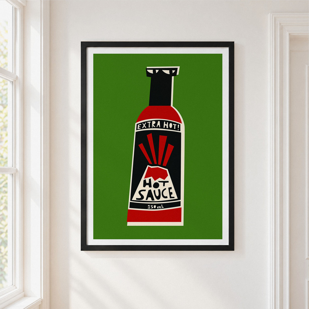 A framed art print of a retro hot sauce bottle on a green background, hung on a white wall next to a window.