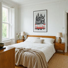 A framed art print featuring a black and white architectural illustration of Istanbul with a red tram, styled Above a wooden bed