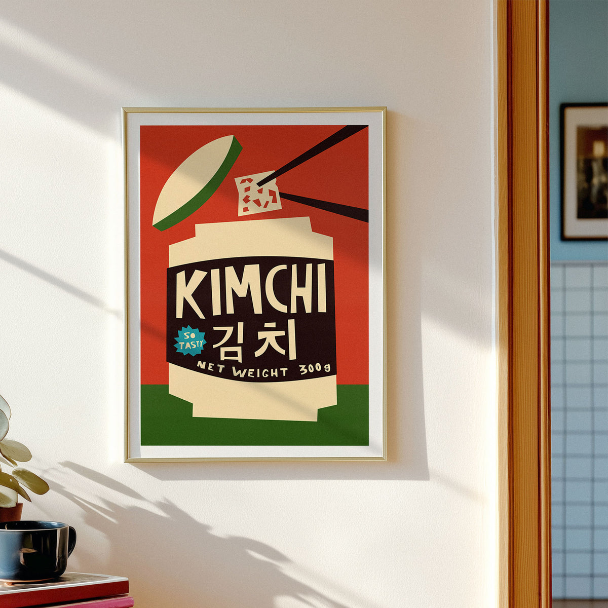 A framed art print featuring a retro-style illustration of Kimchi with Korean text, hanging on a white wall in a modern interior setting.