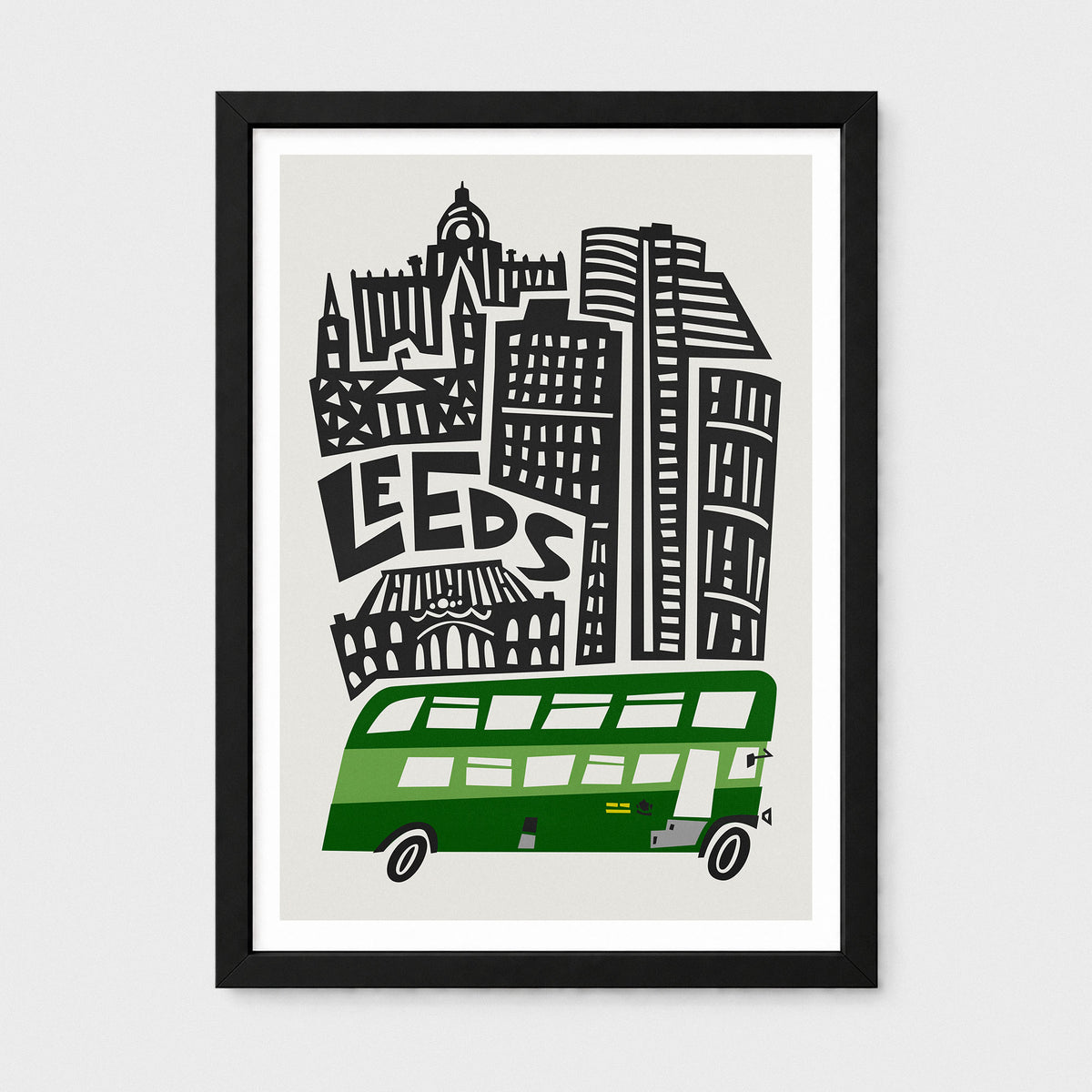 Framed art print featuring a stylized black and white cityscape with the word 'LEEDS' and a green double-decker bus on a light gray background, shown in a black frame against a light gray wall.