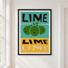 A framed art print featuring a retro-style lime illustration with the word 'LIME' in bold black letters on a teal and mustard yellow background, hung on a white wall next to a window.