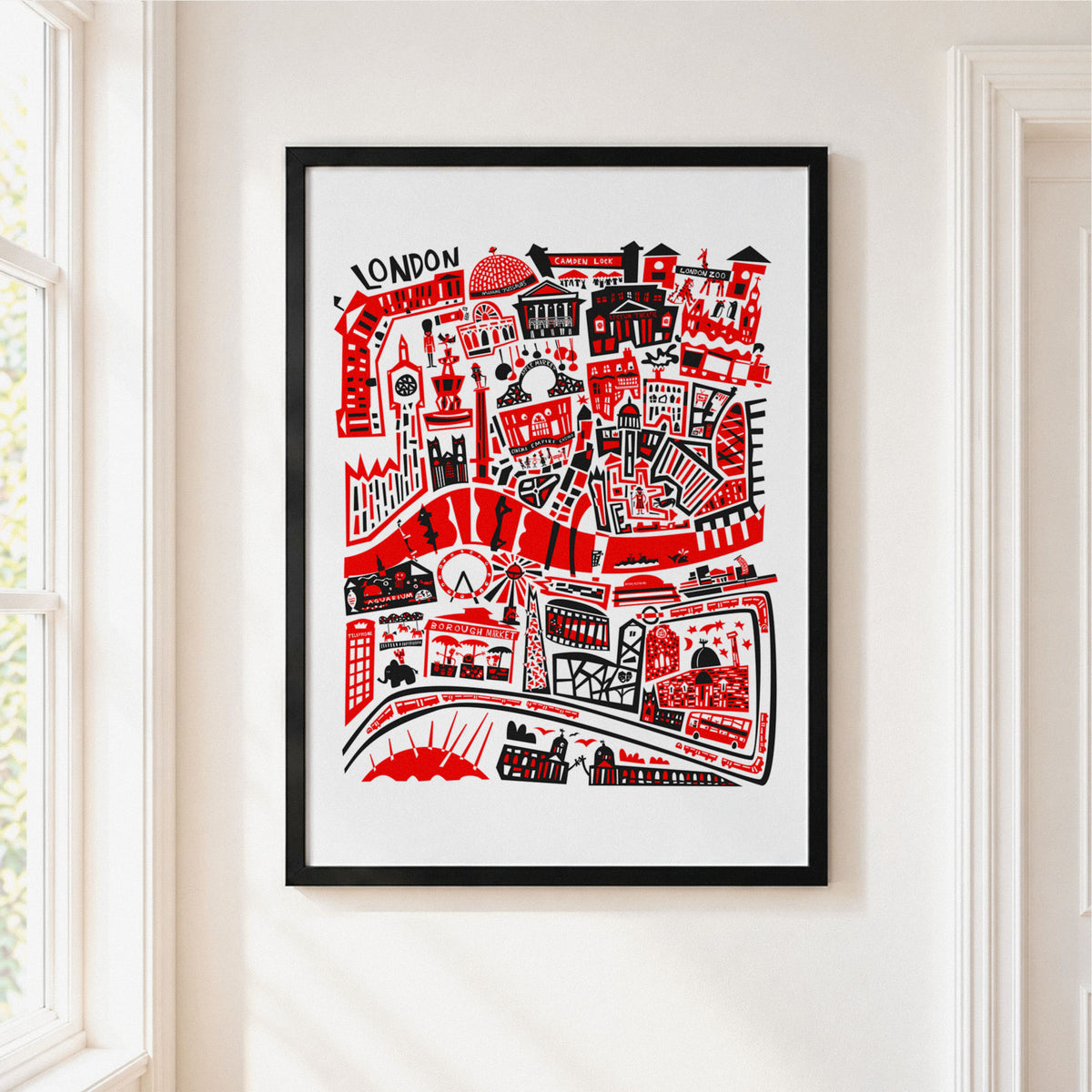 A framed art print featuring a red and black hand-drawn London cityscape with iconic landmarks, hung on a white wall next to a window.