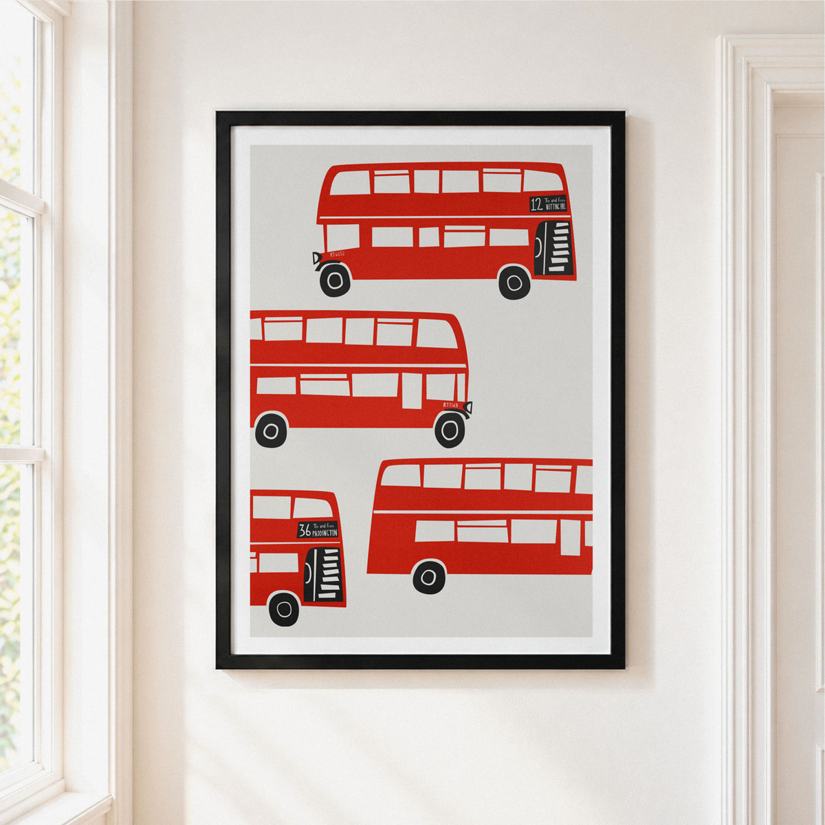 London red bus illustration in a black frame on a cream white wall near a window.