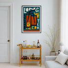 A framed vertical art print featuring a colorful retro-style illustration of a long island iced tea glass, displayed on a white wall in a modern living room setting above a wooden bar cart.