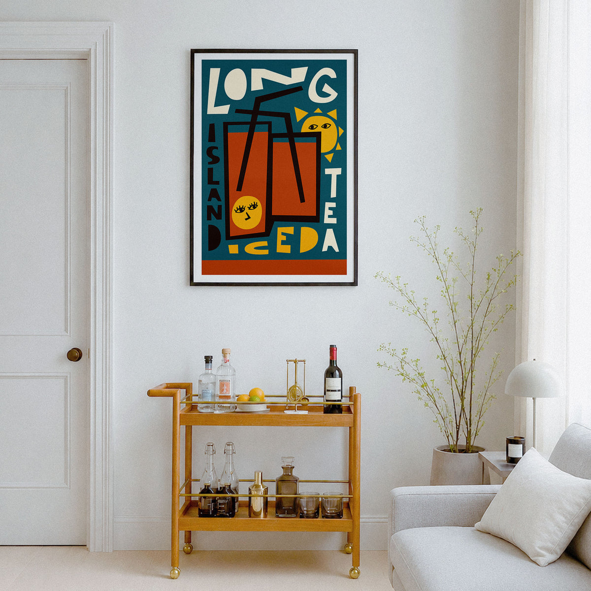 A framed vertical art print featuring a colorful retro-style illustration of a long island iced tea glass, displayed on a white wall in a modern living room setting above a wooden bar cart.