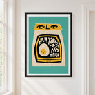 A framed art print featuring a stylized mayonnaise jar illustration with a cream-colored body, black label, yellow accents, and a teal background, hung on a white wall next to a window.
